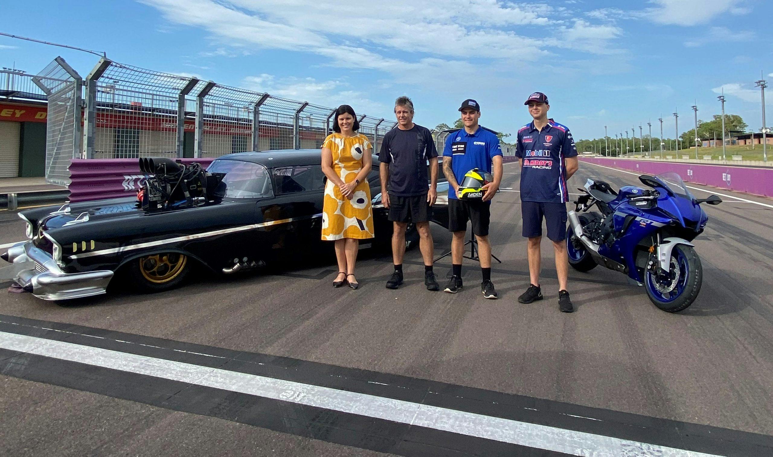 Group of people standing in front of a drag car and Superbike